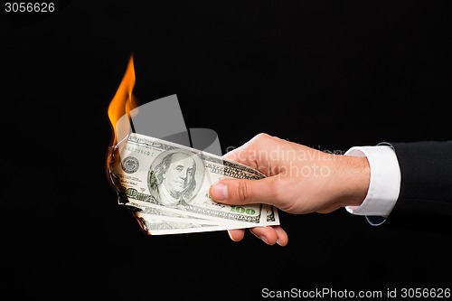 Image of close up of male hand holding burning dollar money