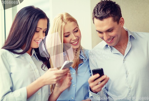 Image of smiling business team with smartphones in office