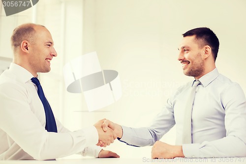 Image of two smiling businessmen shaking hands in office