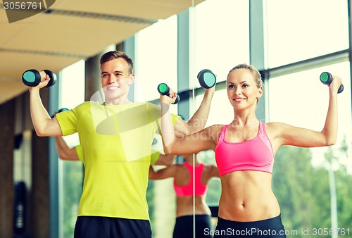 Image of smiling man and woman with dumbbells in gym