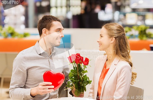 Image of happy couple with present and flowers in mall