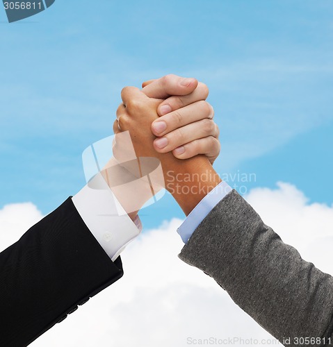 Image of close up of hands armwrestling over concrete wall