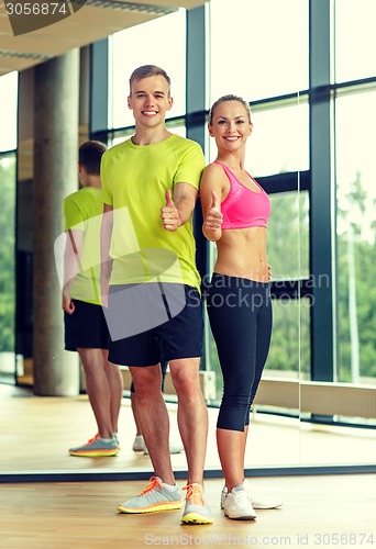 Image of smiling man and woman showing thumbs up in gym