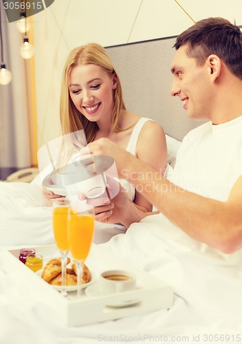 Image of smiling couple having breakfast in bed in hotel