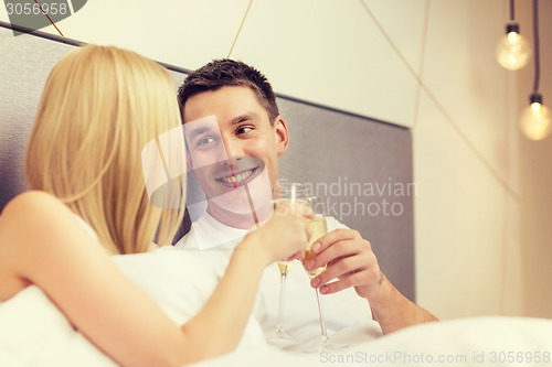 Image of smiling couple with champagne glasses in bed