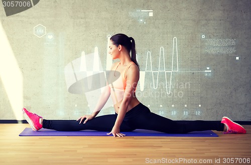 Image of smiling woman stretching leg on mat in gym