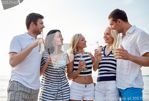 Image of smiling friends with drinks in bottles on beach