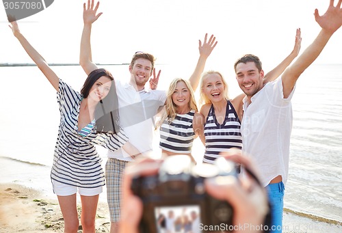 Image of friends on beach waving hands and photographing