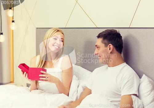 Image of smiling couple in bed with red gift box