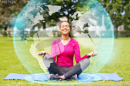 Image of smiling woman meditating on mat outdoors