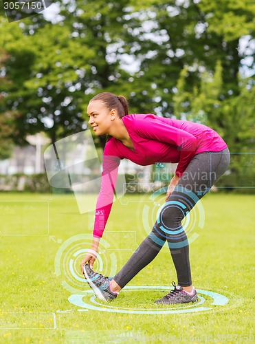 Image of smiling woman stretching leg outdoors