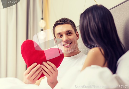 Image of smiling couple in bed with red heart shape pillow