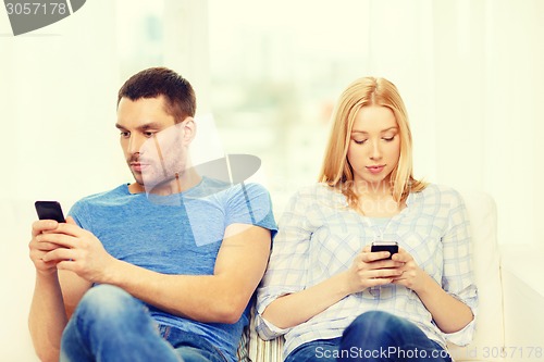 Image of concentrated couple with smartphones at home