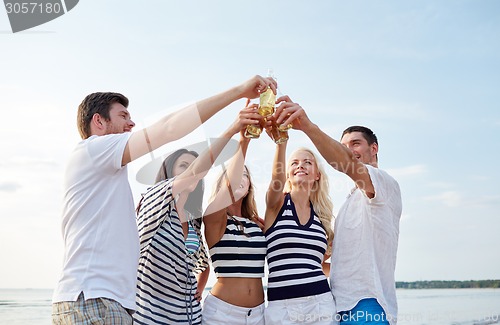 Image of smiling friends clinking bottles on beach