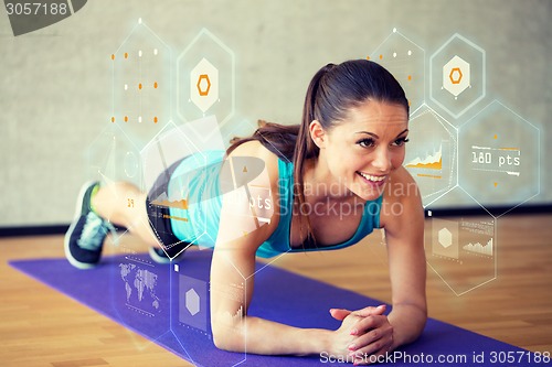 Image of smiling woman doing exercises on mat in gym