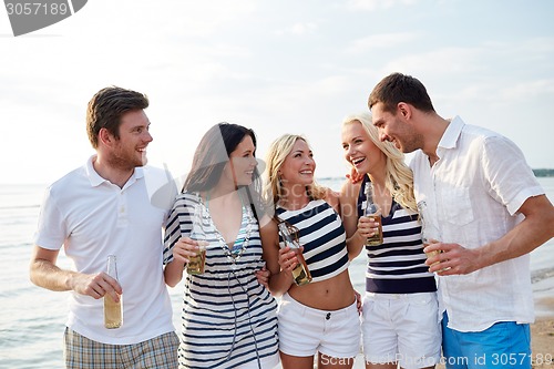 Image of smiling friends with drinks in bottles on beach