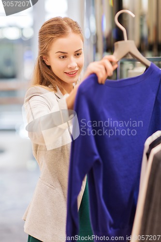 Image of happy young woman choosing clothes in mall