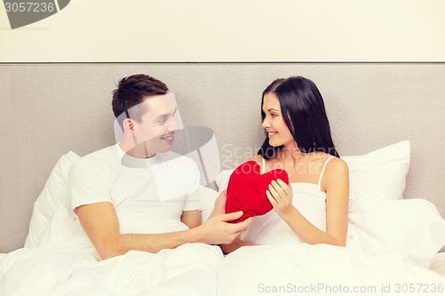 Image of smiling couple in bed with red heart shape pillow