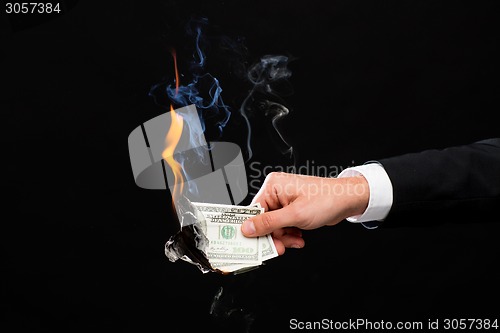 Image of close up of male hand holding burning dollar money