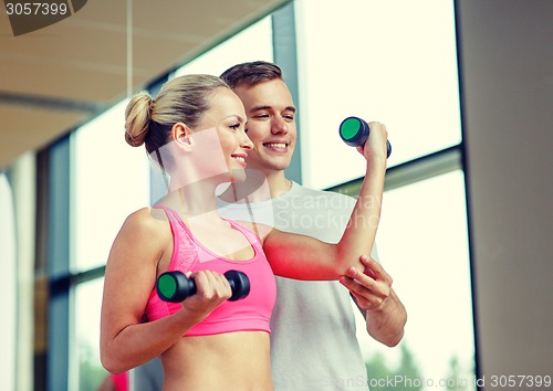 Image of smiling young woman with personal trainer in gym