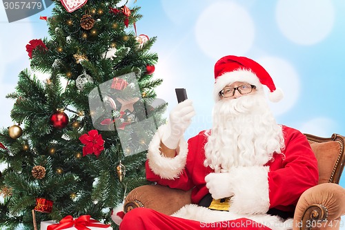 Image of santa claus with smartphone and christmas tree