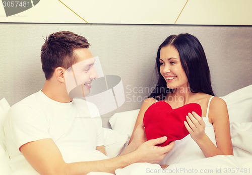 Image of smiling couple in bed with red heart shape pillow