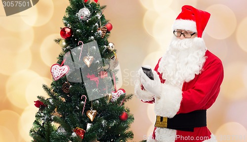 Image of santa claus with smartphone and christmas tree