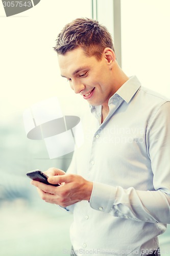Image of smiling businessman with smartphone in office