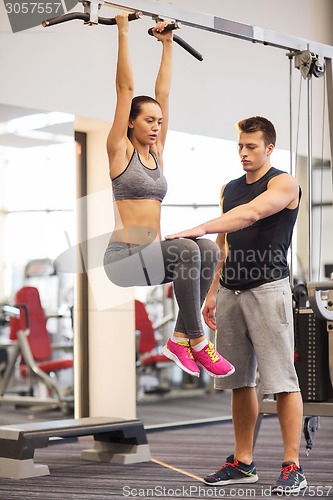 Image of young woman with trainer doing leg raises in gym