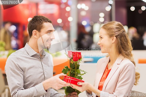 Image of happy couple with present and flowers in mall