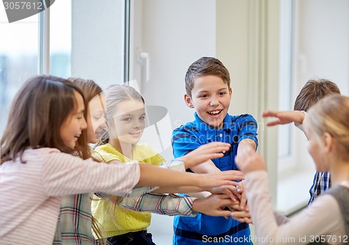 Image of group of smiling school kids putting hands on top