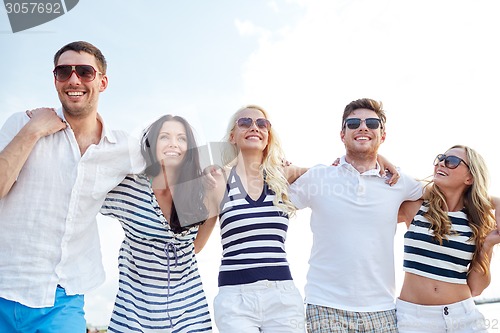 Image of smiling friends in sunglasses walking on beach