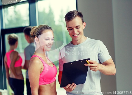 Image of smiling young woman with personal trainer in gym