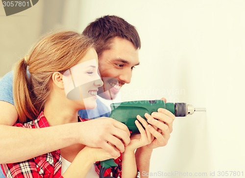 Image of smiling couple drilling hole in wall at home