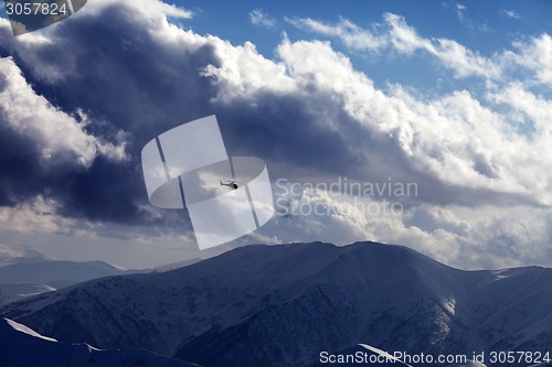 Image of Helicopter in cloudy sky and winter mountains in evening