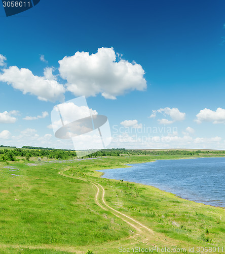 Image of green landscape with road and pond under blue sky with white clo