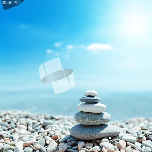 Image of zen-like stones on beach and sun in sky