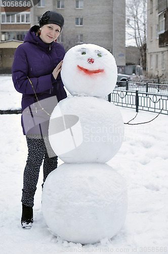 Image of The woman near a snowman in the yard of the house.