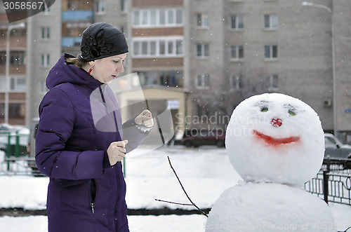 Image of The woman near a snowman in the yard of the house.