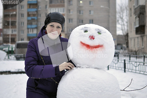 Image of The woman near a snowman in the yard of the house.
