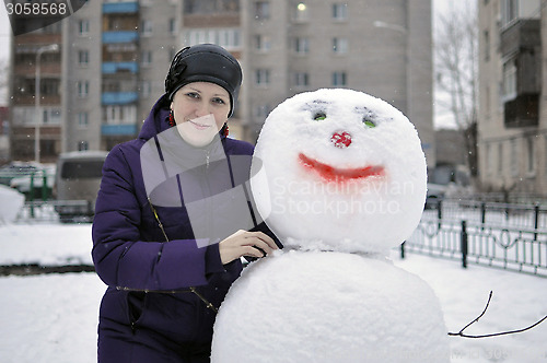 Image of The woman near a snowman in the yard of the house.