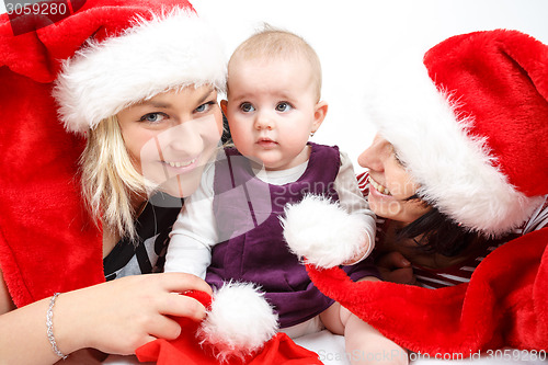 Image of smiling infant baby with two womans with santa hats