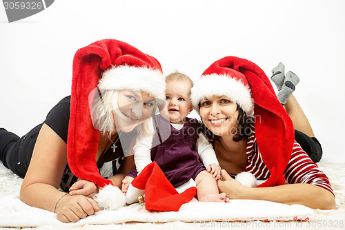 Image of smiling infant baby with two womans with santa hats