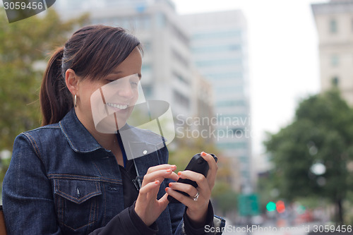 Image of Woman texting with her smart phone outside in the city