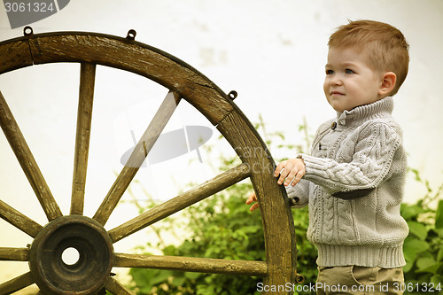 Image of 2 years old curious Baby boy with old wooden wheel 
