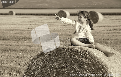 Image of small rural girl on the straw after harvest field with straw bal