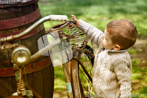 Image of 2 years old curious Baby boy walking around the old bike 