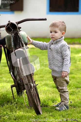 Image of 2 years old curious Baby boy walking around the old bike 