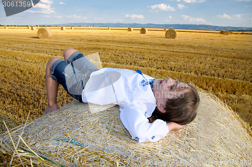 Image of small rural girl on the straw after harvest field with straw bal
