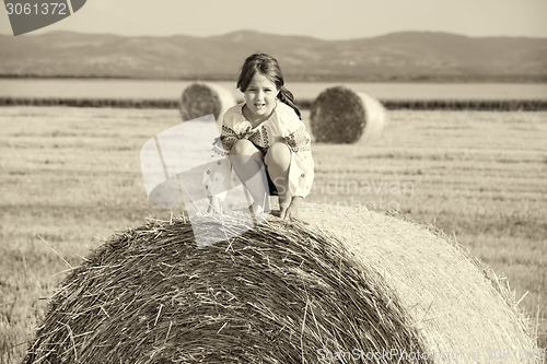 Image of small rural girl on the straw after harvest field with straw bal